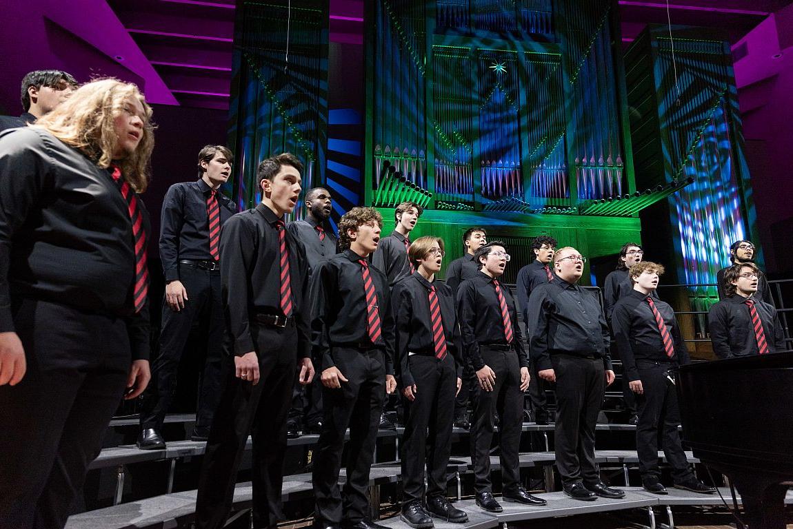 A group of men in black dress cloths singing.